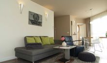 Das modern eingerichtete Wohnzimmer mit gemütlicher Couchgarnitur, Essecke und Zugang zur möblierten Terrasse